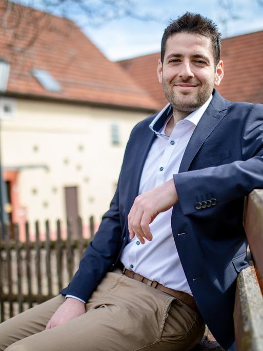 Bürgermeister Ryyan Alshebl sitzt auf einer Bank im schwäbischen Ort Ostelsheim. Er stützt den Linken Arm auf die Lehne, lächelt und blickt direkt in die Kamera.