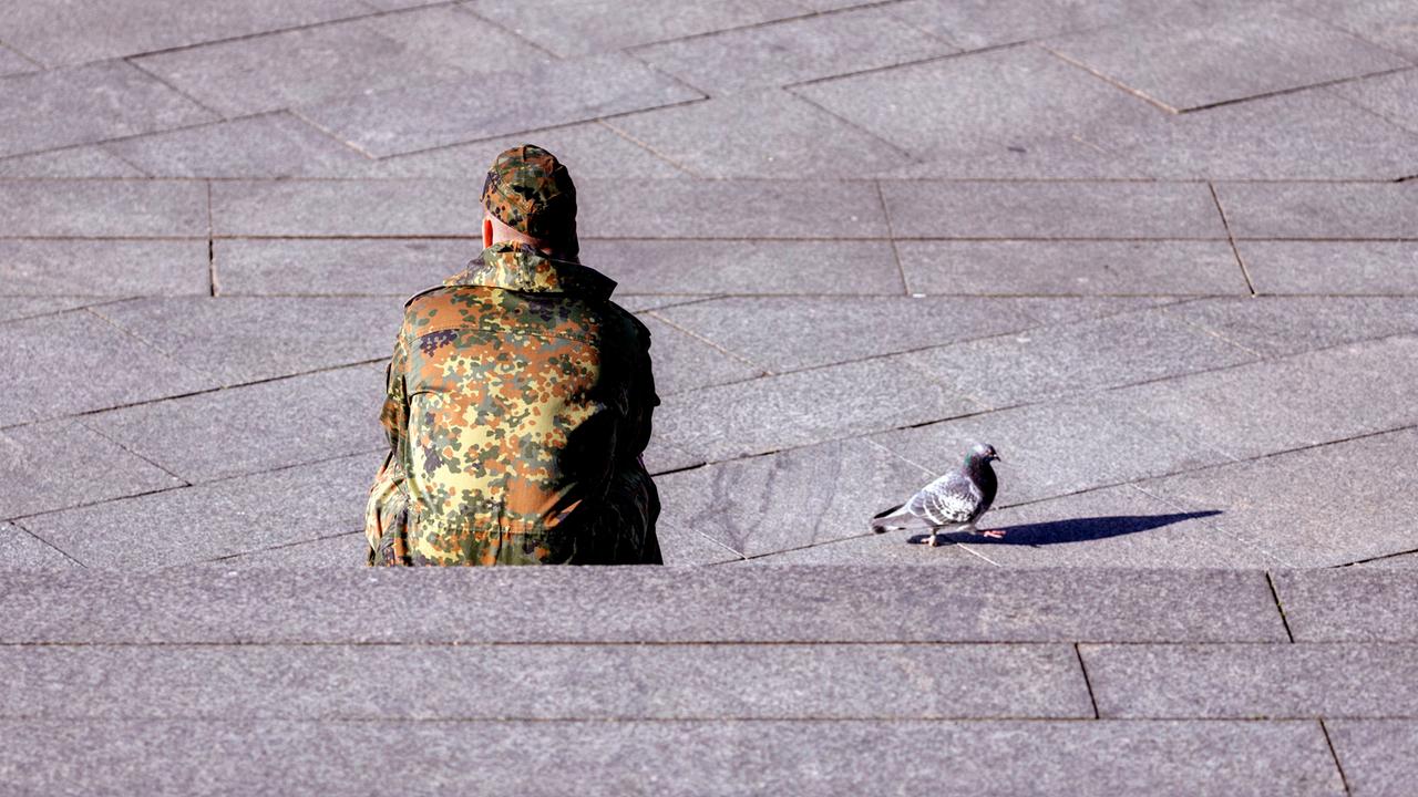 Ein Bundeswehr-Soldat sitzt auf einer Treppe, neben ihm läuft eine Taube.