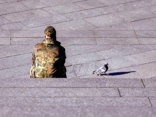 Ein Bundeswehr-Soldat sitzt auf einer Treppe, neben ihm läuft eine Taube.