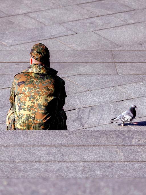 Ein Bundeswehr-Soldat sitzt auf einer Treppe, neben ihm läuft eine Taube.