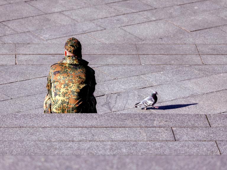 Ein Bundeswehr-Soldat sitzt auf einer Treppe, neben ihm läuft eine Taube.