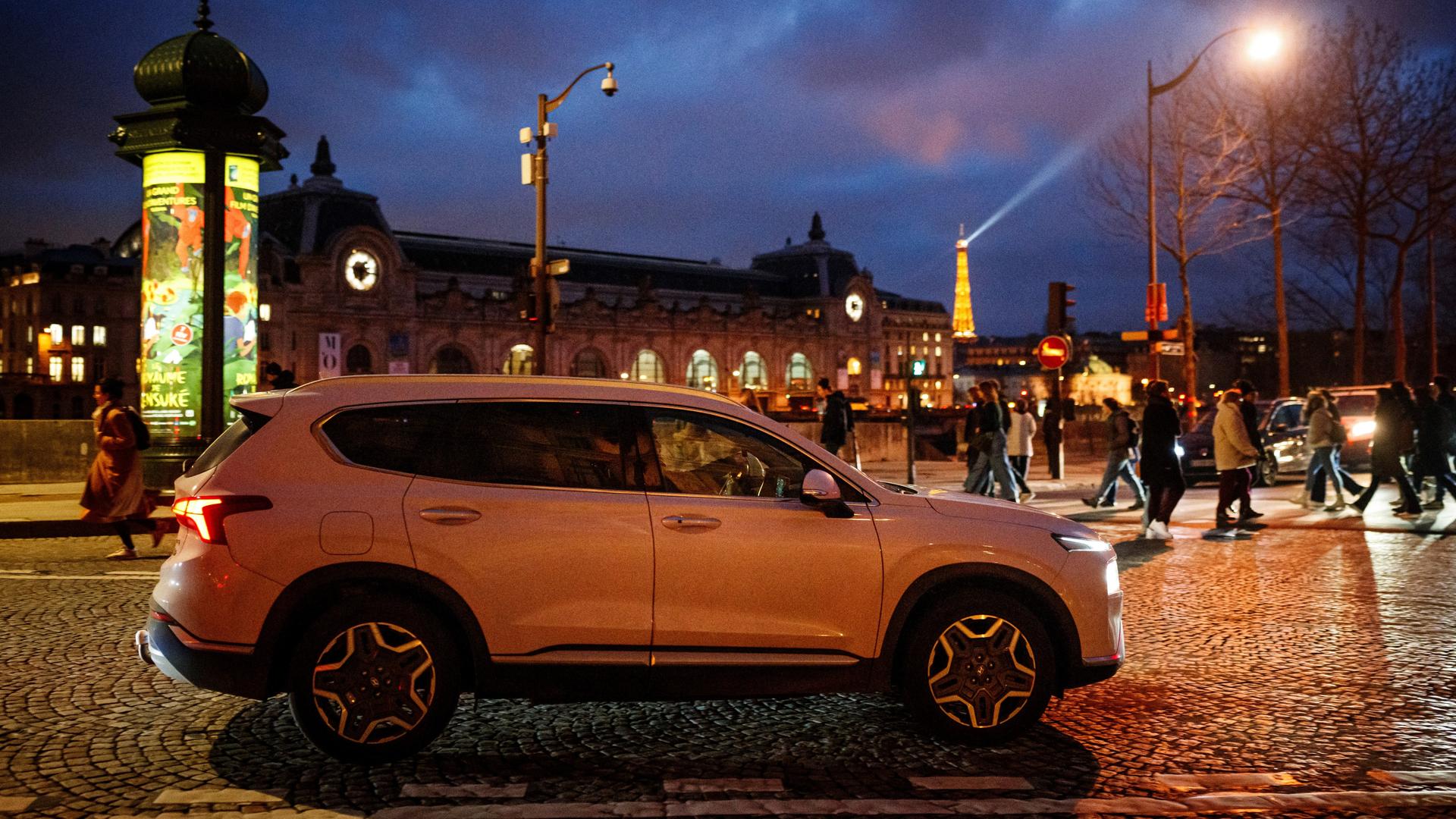 Das Foto zeigt einen großen Pkw in Paris, es ist Abend, im Hintergrund leuchtet der Eiffelturm.