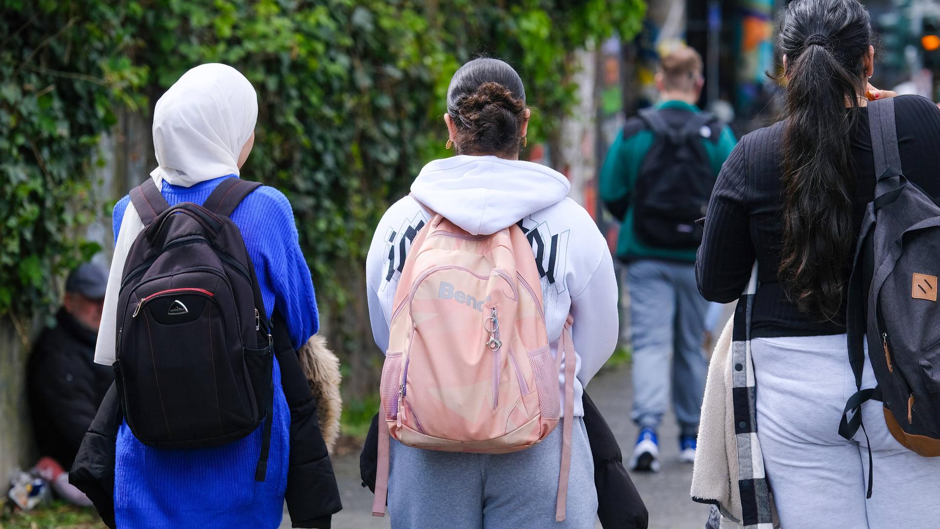 Jugendliche mit Schulranzen und Rucksack auf dem Schulweg. Das Mädchen links auf dem Bild trägt ein Kopftuch.