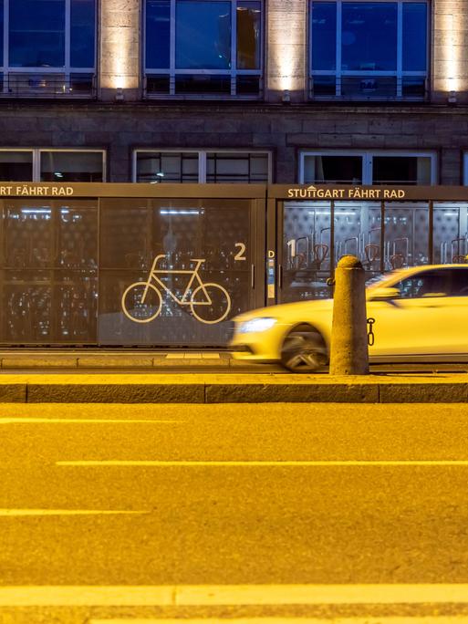 Vor dem Hauptbahnhof in Stuttgart stehen zwei Container, in die Fahrräder in einzelnen Boxen abgestellt werden können. Es ist dunkel. Auf der Straße davor fährt ein Taxi (14.06.2021)