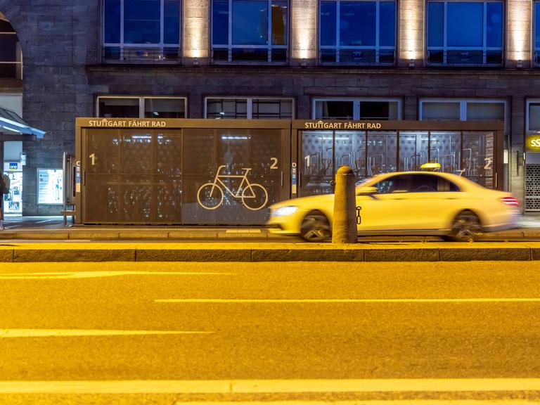 Vor dem Hauptbahnhof in Stuttgart stehen zwei Container, in die Fahrräder in einzelnen Boxen abgestellt werden können. Es ist dunkel. Auf der Straße davor fährt ein Taxi (14.06.2021)