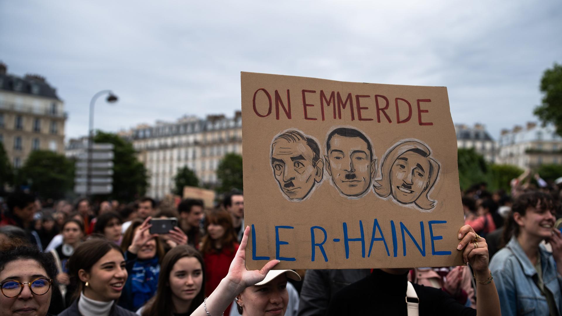 Protest gegen rechts in Frankreich, ein Schild zeigt die Köpfe von Rassemblement-Politikern mit Hitlerbärten und der Aufschrift ''On emmerde le R-Haine''