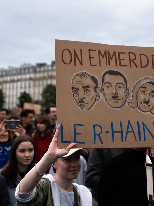 Protest gegen rechts in Frankreich, ein Schild zeigt die Köpfe von Rassemblement-Politikern mit Hitlerbärten und der Aufschrift ''On emmerde le R-Haine''