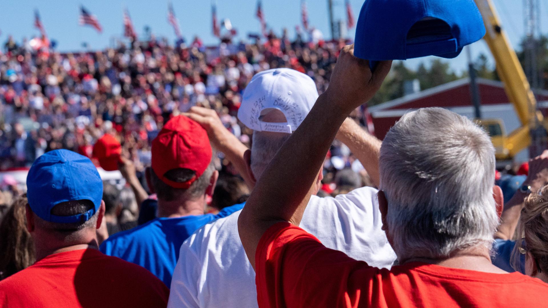 Mehrere Personen mit Baseballkappen in den amerikanischen Farben fotografiert von hinten, bei einer Trump-Veranstaltung in Butler, Pennsylvania.