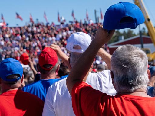 Mehrere Personen mit Baseballkappen in den amerikanischen Farben fotografiert von hinten, bei einer Trump-Veranstaltung in Butler, Pennsylvania.