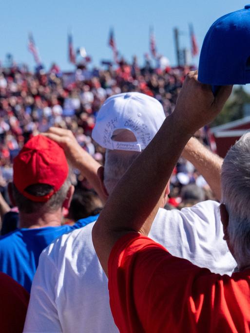 Mehrere Personen mit Baseballkappen in den amerikanischen Farben fotografiert von hinten, bei einer Trump-Veranstaltung in Butler, Pennsylvania.