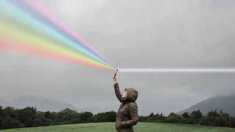 Eine Person steht auf einer Wiese und hält eine Lupe in die Luft in der weißes Licht zum Regenbogenspektrum gebrochen wird.