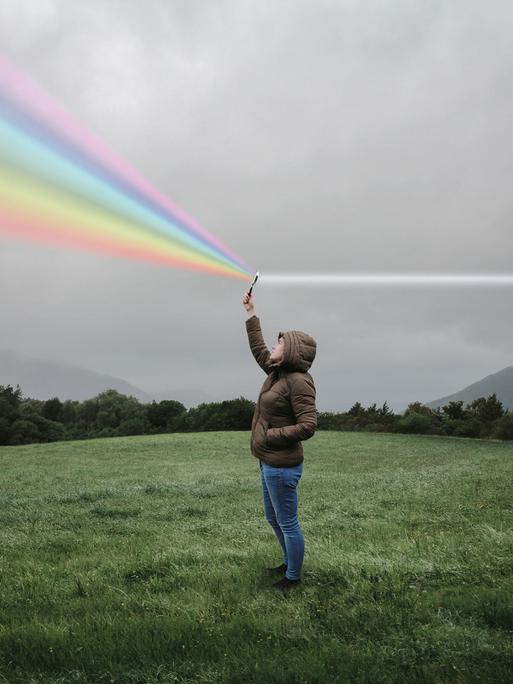 Eine Person steht auf einer Wiese und hält eine Lupe in die Luft in der weißes Licht zum Regenbogenspektrum gebrochen wird.