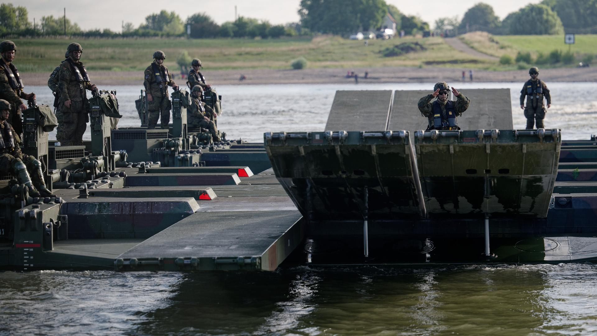 Amphibienfahrzeuge der Bundeswehr bilden eine Fähre auf dem Rhein, darauf stehen Soldaten. 