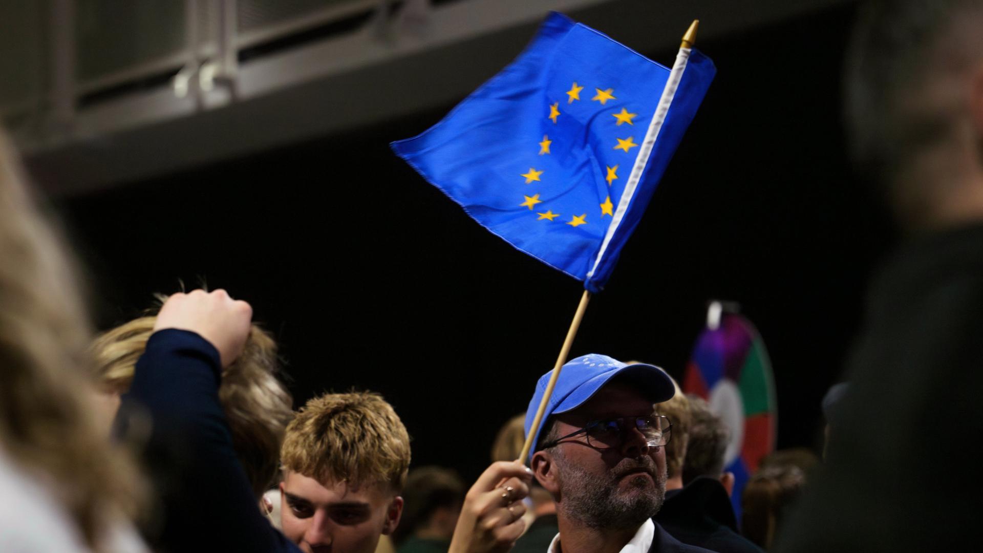 Eine Veranstaltung von Unterstützern für den Beginn von Beitrittsgesprächen mit der EU. Menschen stehen zusammen. Eine Person schwenkt eine blaue EU-Fahne mit den gelben Sternen.