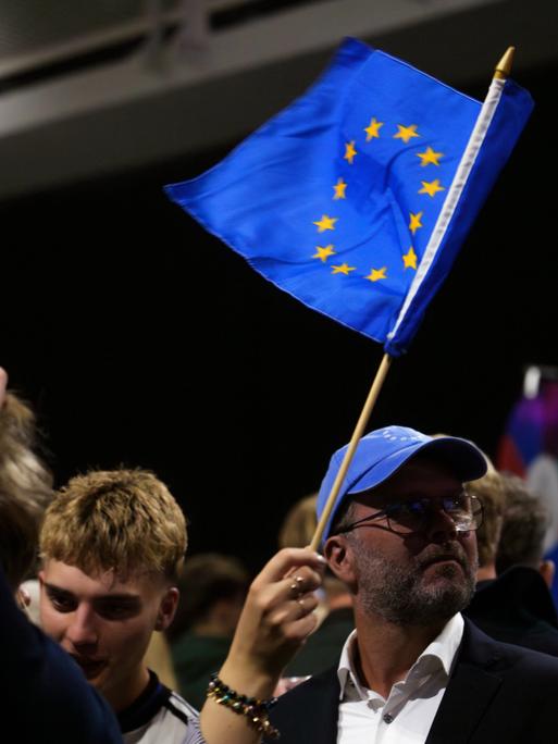 Eine Veranstaltung von Unterstützern für den Beginn von Beitrittsgesprächen mit der EU. Menschen stehen zusammen. Eine Person schwenkt eine blaue EU-Fahne mit den gelben Sternen. Eine Veranstaltung von Unterstützern für den Beginn von Beitrittsgesprächen mit der EU. Menschen stehen zusammen. Eine Person schwenkt eine blaue EU-Fahne mit den gelben Sternen.