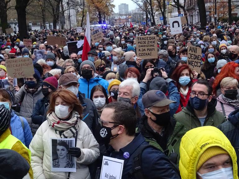 Tausende Menschen mit Plakaten auf einer Straße, dicht gedrängt, mit Masken.