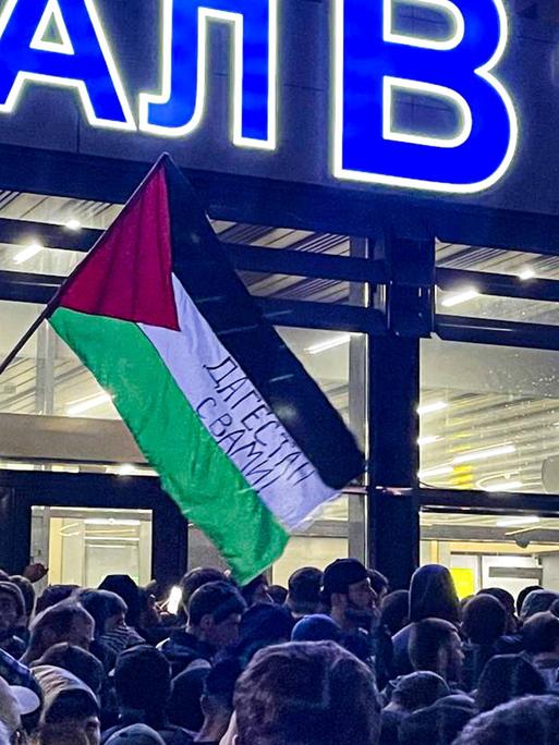 Hunderte Menschen versammeln sich vor dem Flughafen. Ein Mann schwenkt eine palästinensische Flagge.