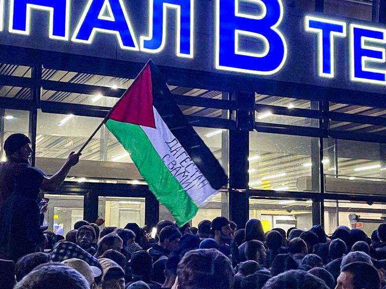 Hunderte Menschen versammeln sich vor dem Flughafen. Ein Mann schwenkt eine palästinensische Flagge.