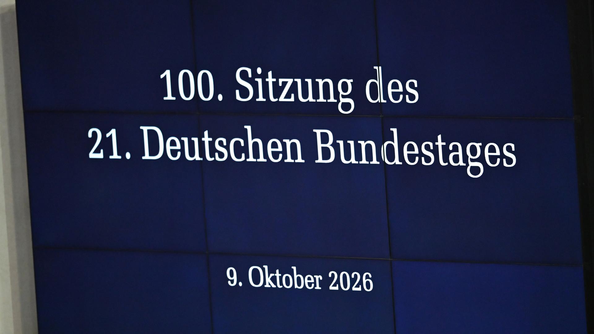 Auf einer Anzeigetafel im Plenum des Bundestags ist der Schriftzug "100. Sitzung des 21. Deutschen Bundestags - 9. Oktober 2026" zu lesen. Auf einer Anzeigetafel im Plenum des Bundestags ist der Schriftzug "100. Sitzung des 21. Deutschen Bundestags - 9. Oktober 2026" zu lesen.