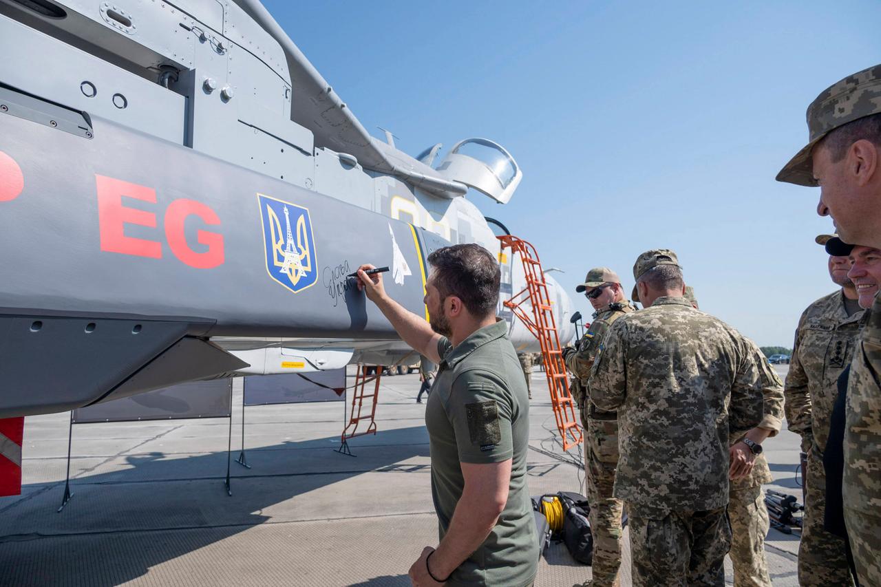 Der ukrainische Präsident Selenskyj unterschreibt auf einem Flugplatz einen Marschflugkörper vom Typ "Storm Shadow/SCALP-EG ". Darauf ist ein Eiffelturm zu sehen.