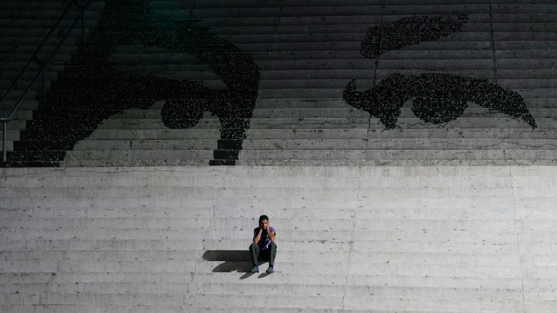 Ein Mann sitzt auf einer Treppe. Auf den Treppen ist ein Graffiti, das die Augen des verstorbenen venezuelanischen Präsidenten Hugo Chavez zeigen.