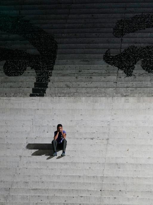 Ein Mann sitzt auf einer Treppe. Auf den Treppen ist ein Graffiti, das die Augen des verstorbenen venezuelanischen Präsidenten Hugo Chavez zeigen.