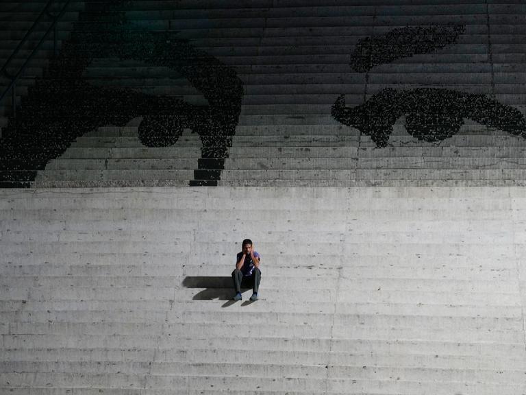 Ein Mann sitzt auf einer Treppe. Auf den Treppen ist ein Graffiti, das die Augen des verstorbenen venezuelanischen Präsidenten Hugo Chavez zeigen.