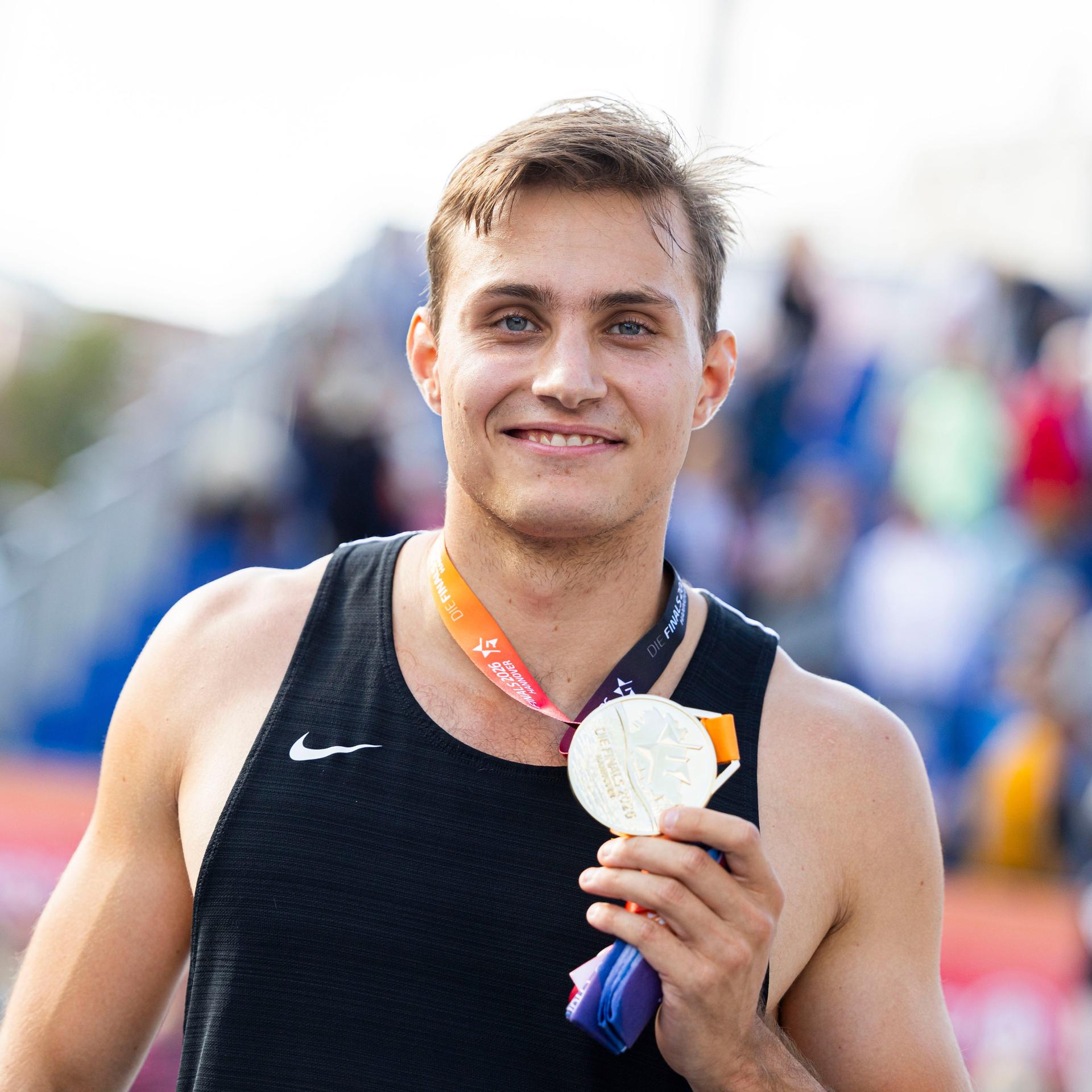 Marec Metzger hält die Goldmedaille zur Deutschen Meisterschaft im Stabhochsprung in seiner Hand. Er strahlt.  