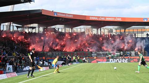 Blick in das Stadion von Eintracht Braunschweig. Im Hintergrund zünden Hannovers Fans Pyrotechnik.