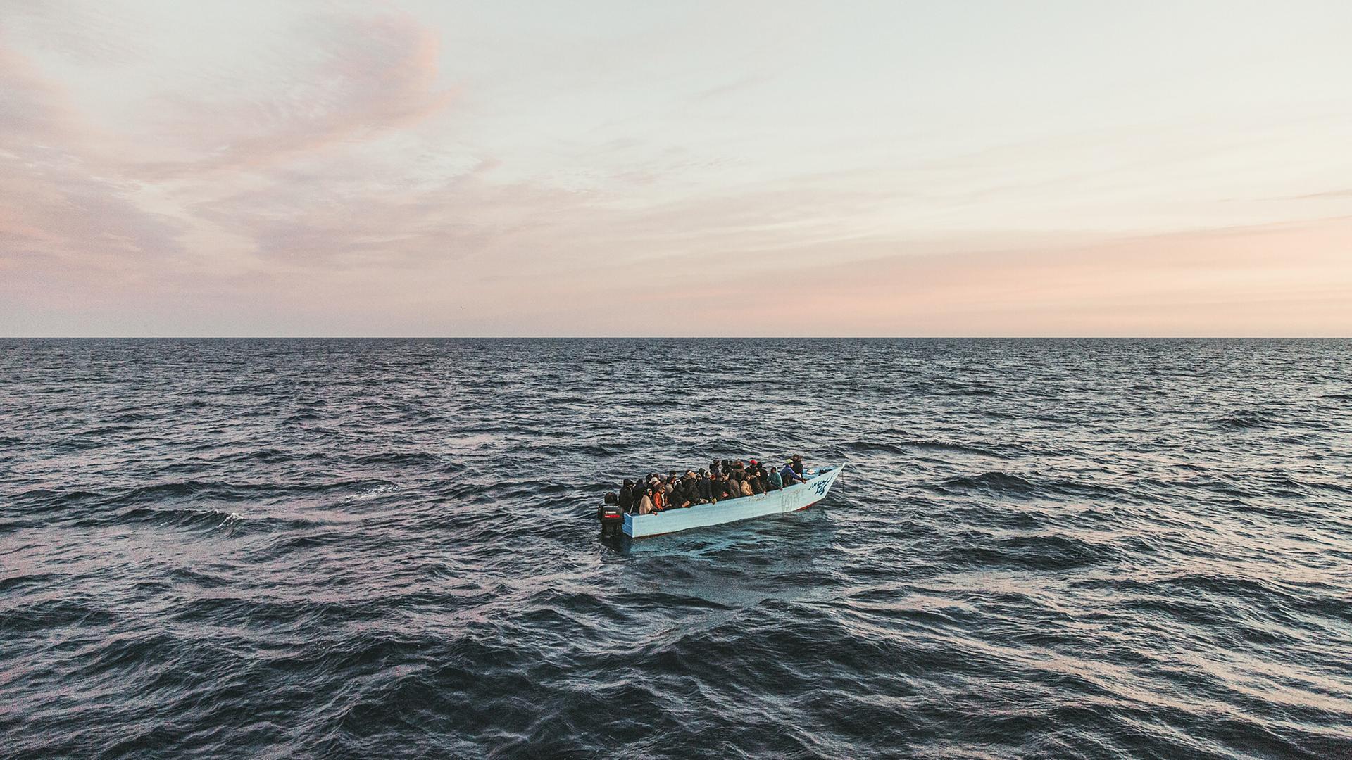 Blick auf ein Fischerboot auf dem Meer mit über vierzig Menschen an Bord bei Sonnenaufgang Blick auf ein Fischerboot auf dem Meer mit über vierzig Menschen an Bord bei Sonnenaufgang