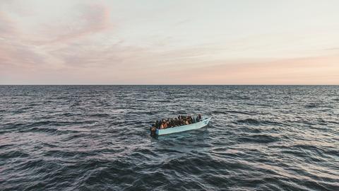 Blick auf ein Fischerboot auf dem Meer mit über vierzig Menschen an Bord bei Sonnenaufgang