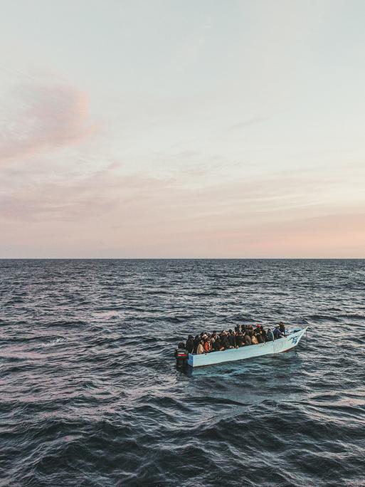 Blick auf ein Fischerboot auf dem Meer mit über vierzig Menschen an Bord bei Sonnenaufgang