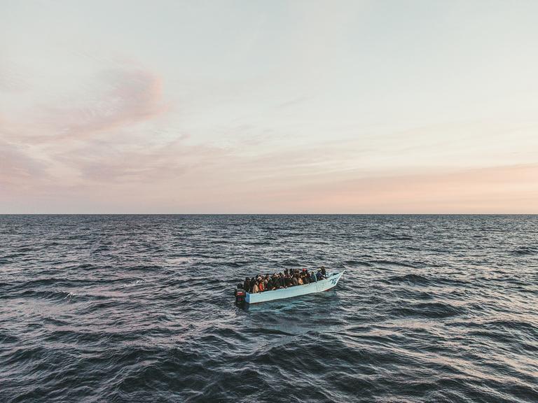 Blick auf ein Fischerboot auf dem Meer mit über vierzig Menschen an Bord bei Sonnenaufgang