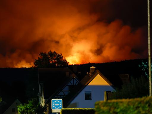 Blick von dem Ortsteil Monschau-Kalterherberg auf die belgische Seite, wo das Hohe Venn in Flammen steht. Der Himmel glüht von den Flammen, im Vordergrund das Schild Belgien und ein Haus. Blick von dem Ortsteil Monschau-Kalterherberg auf die belgische Seite, wo das Hohe Venn in Flammen steht. Der Himmel glüht von den Flammen, im Vordergrund das Schild Belgien und ein Haus.