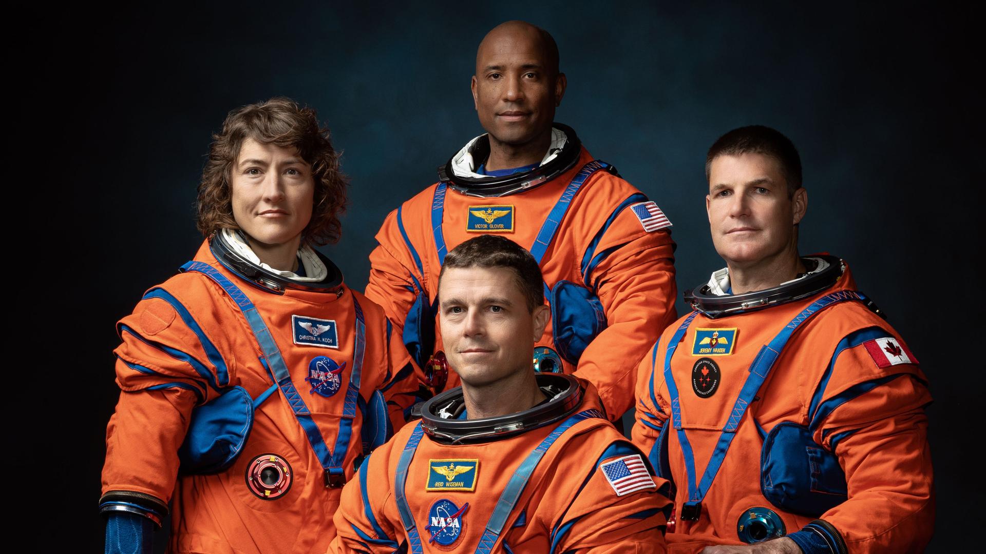 Drei Astronauten und eine Astronautin in orangefarbenen Raumanzügen