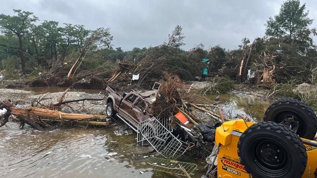 Das Bild zeigt ein zerstörtes Auto. Die Flut hat das Auto mitgerissen. Das Auto liegt zusammen mit anderen zerstörten Dingen im Wasser. 