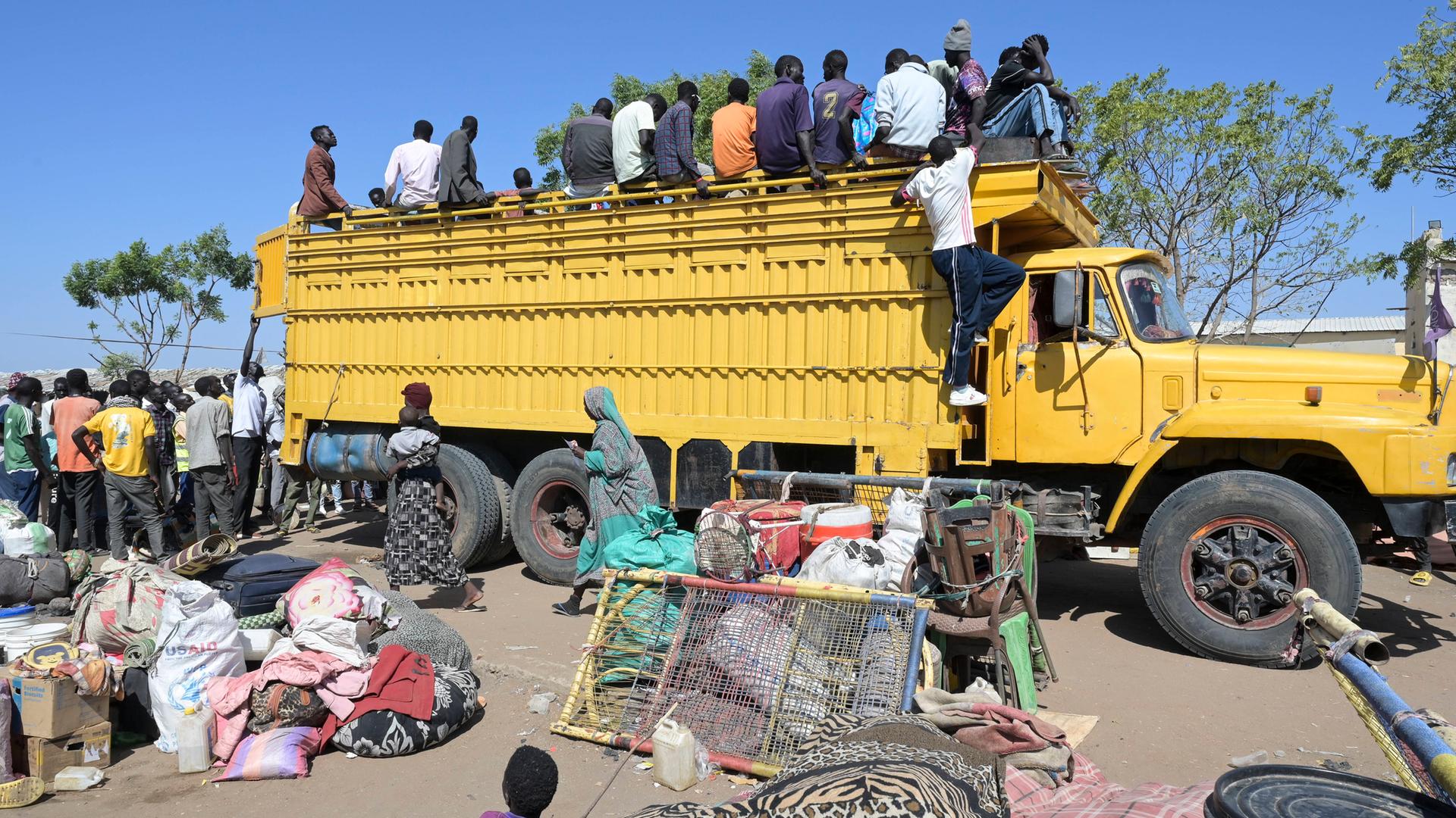Kriegsflüchtlinge im Sudan klettern auf einen gelben Lastkraftwagen.
