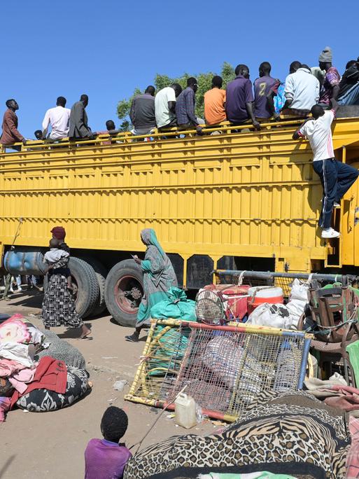 Kriegsflüchtlinge im Sudan klettern auf einen gelben Lastkraftwagen.