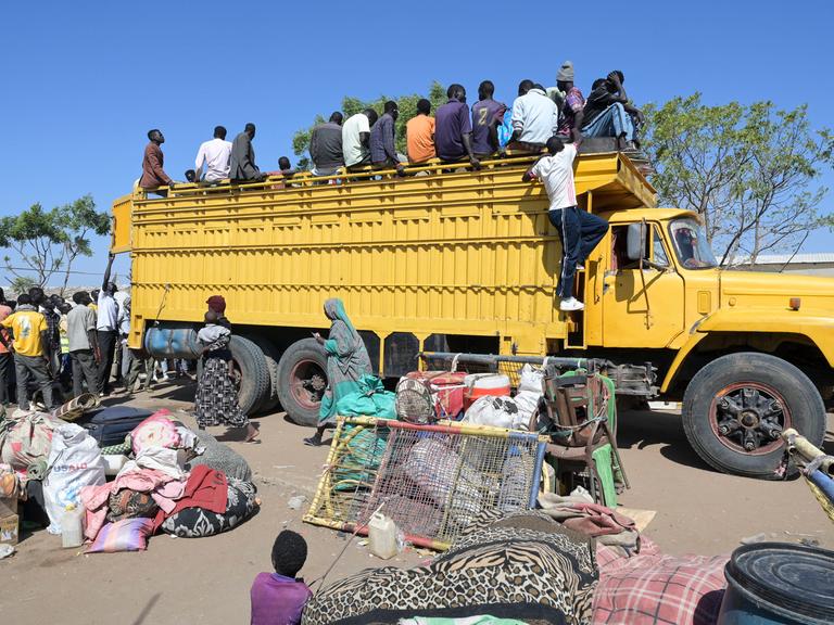 Kriegsflüchtlinge im Sudan klettern auf einen gelben Lastkraftwagen.
