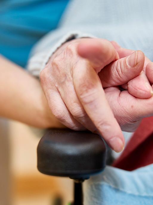 Eine Pflegekraft hält mit einer Bewohnerin in einem Pflegeheim die Hand.