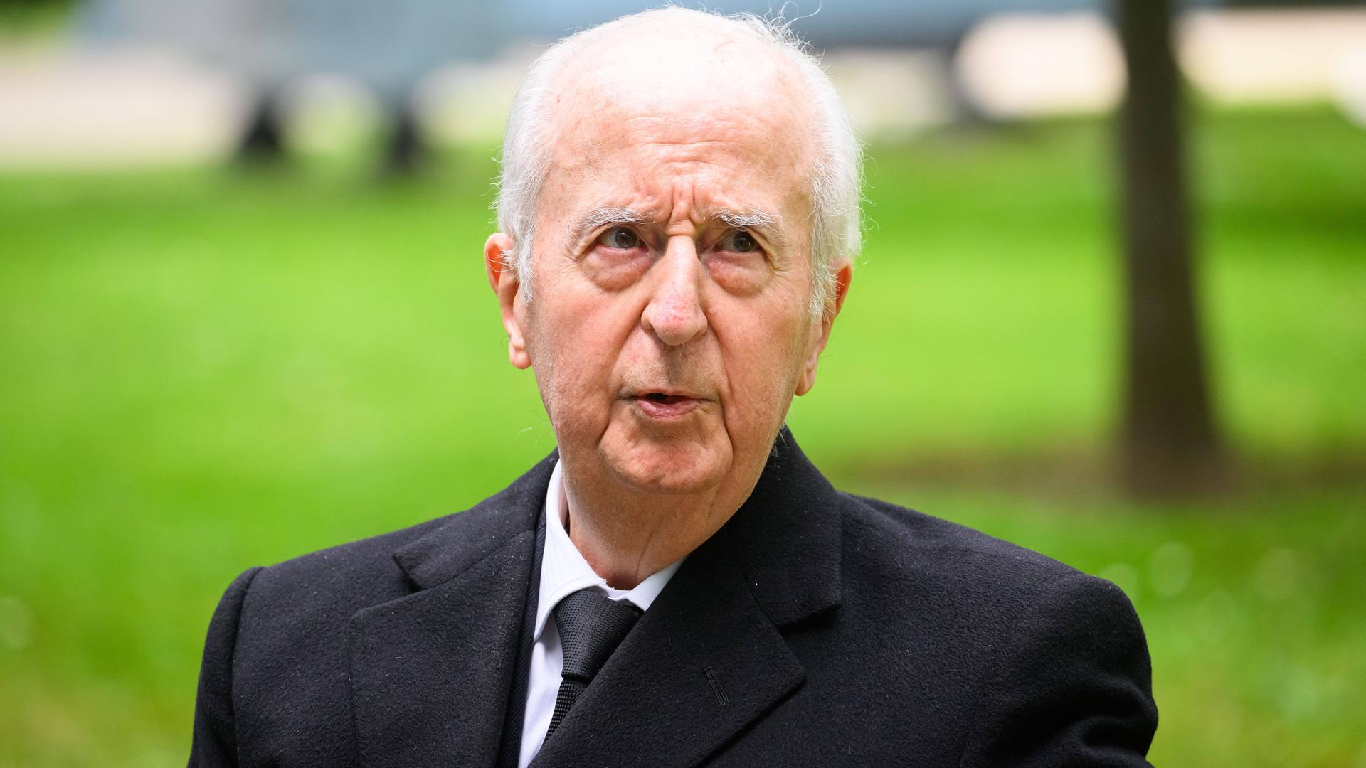 Balladur steht in einem schwarzen Anzug auf einer grünen Wiese.