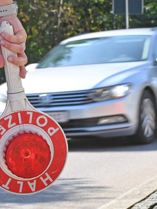 Ein Grenzpolizist hält eine Kelle, im Hintergrund ist ein Auto zu sehen.