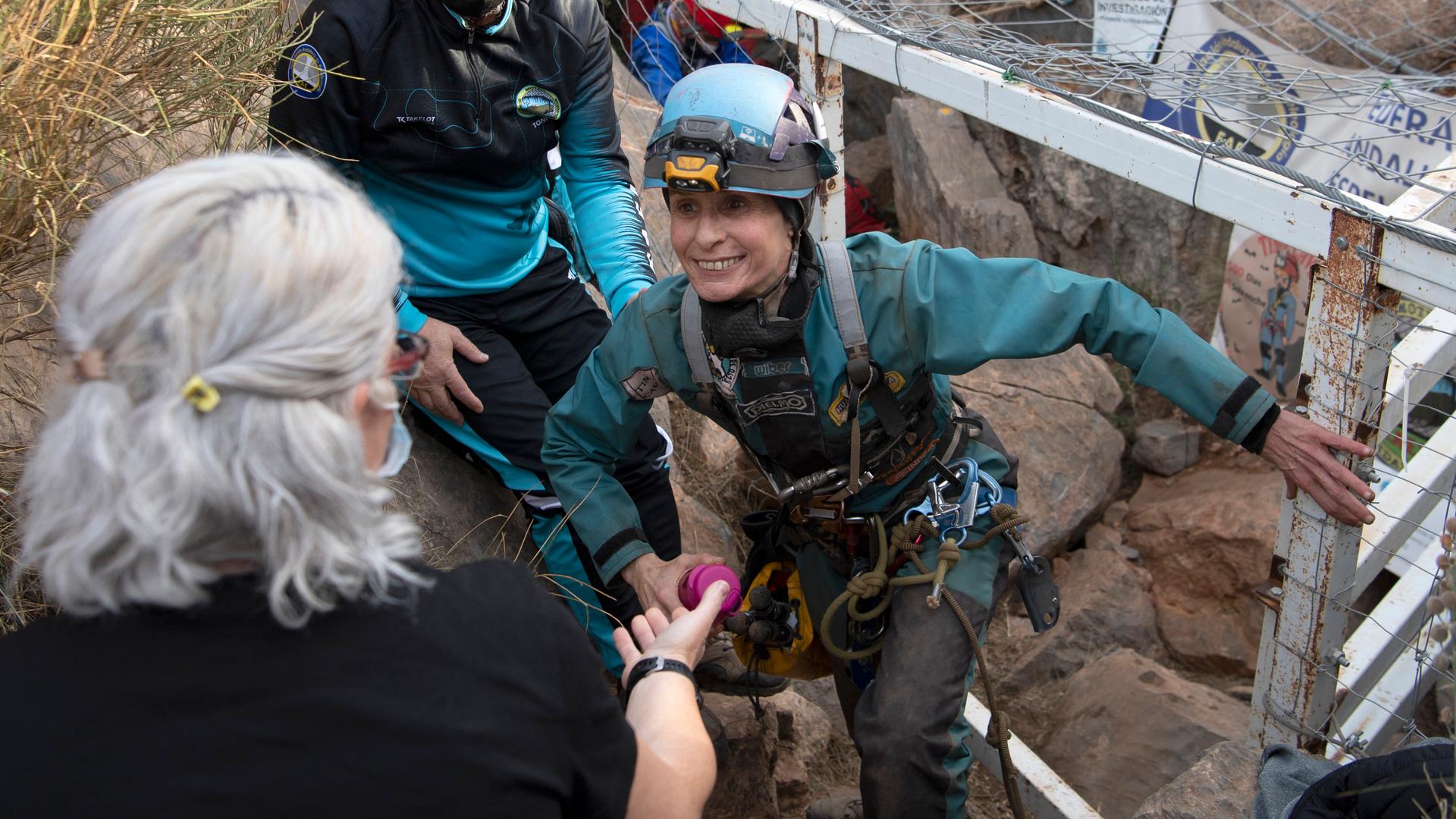 Beatriz Flamini steigt aus der Höhle in Los Gauchos und wird von einer anderen Person empfangen. Sie trägt Schutzkleidung und lächelt. Beatriz Flamini steigt aus der Höhle in Los Gauchos und wird von einer anderen Person empfangen. Sie trägt Schutzkleidung und lächelt.