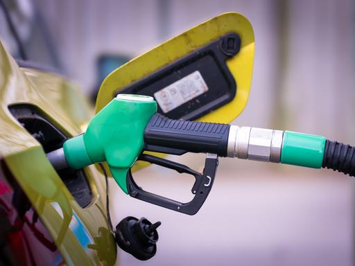 Nahaufnahme einer grünen Zapfpistole, die in den Tankstutzen eines Autos gesteckt ist. Der Tankdeckel ist geöffnet, im Hintergrund ist das Fahrzeug leicht unscharf zu sehen.