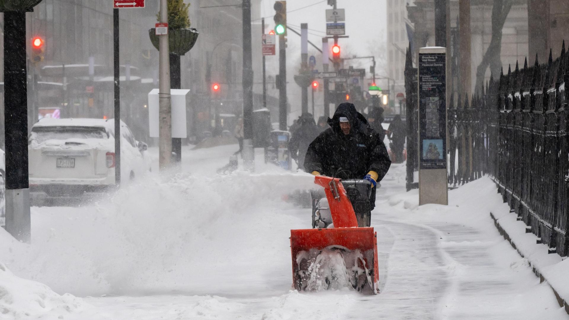 Ein Arbeiter räumt in New York City Schnee von einem Gehweg. Ein Arbeiter räumt in New York City Schnee von einem Gehweg.