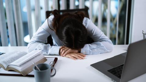 Eine Frau sitzt im Büro am Schreibtisch und hat ihren Kopf auf ihre Arme gelegt