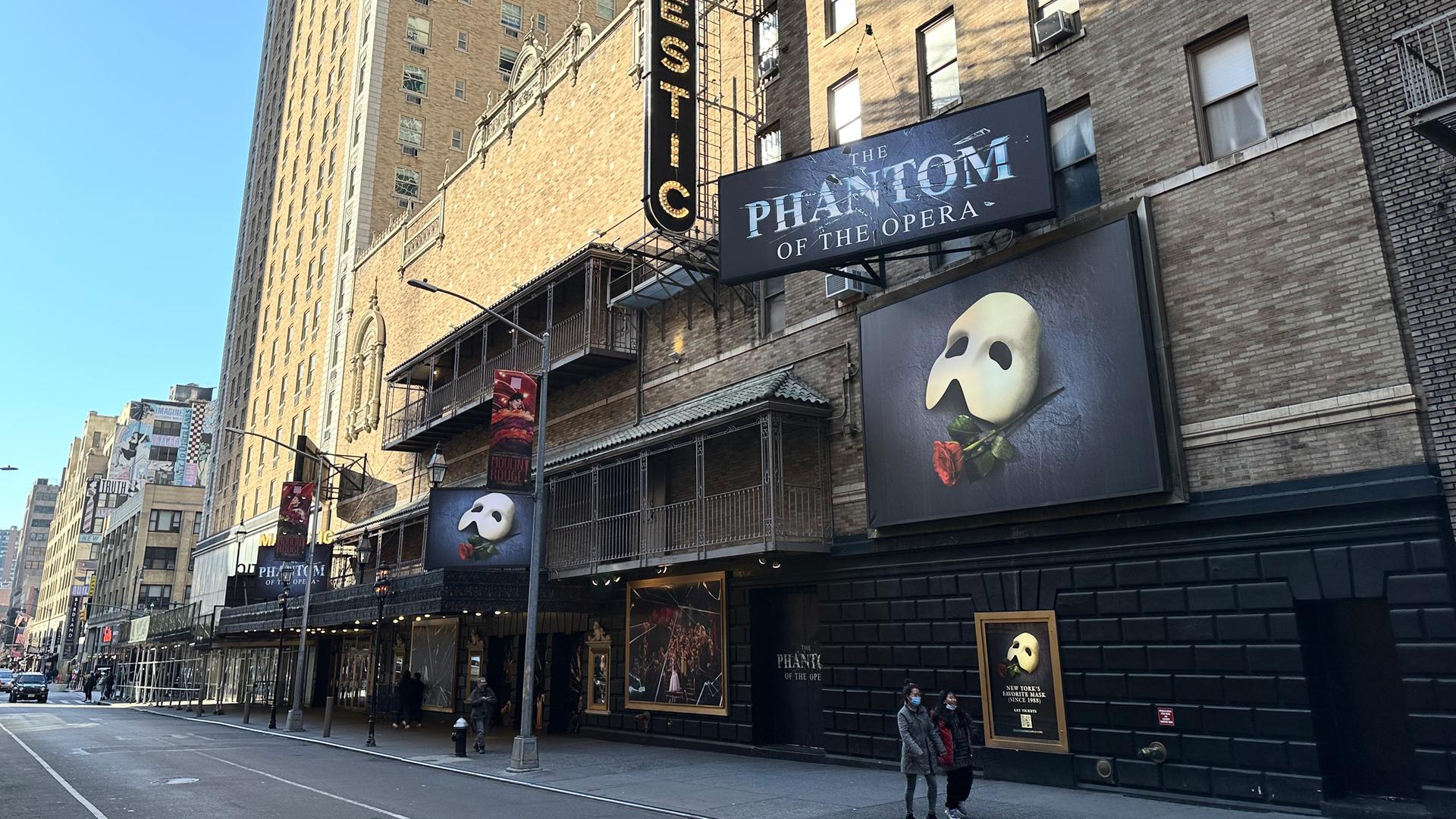 Passanten gehen am Broadway am Majestic Theatre vorbei, in dem nach mehr als 35 Jahren zum letzten Mal «Das Phantom der Oper» gespielt. Außen sind die Plakate des Musicals mit der typischen weißen Gesichtsmaske und einer Rosa zu sehen.