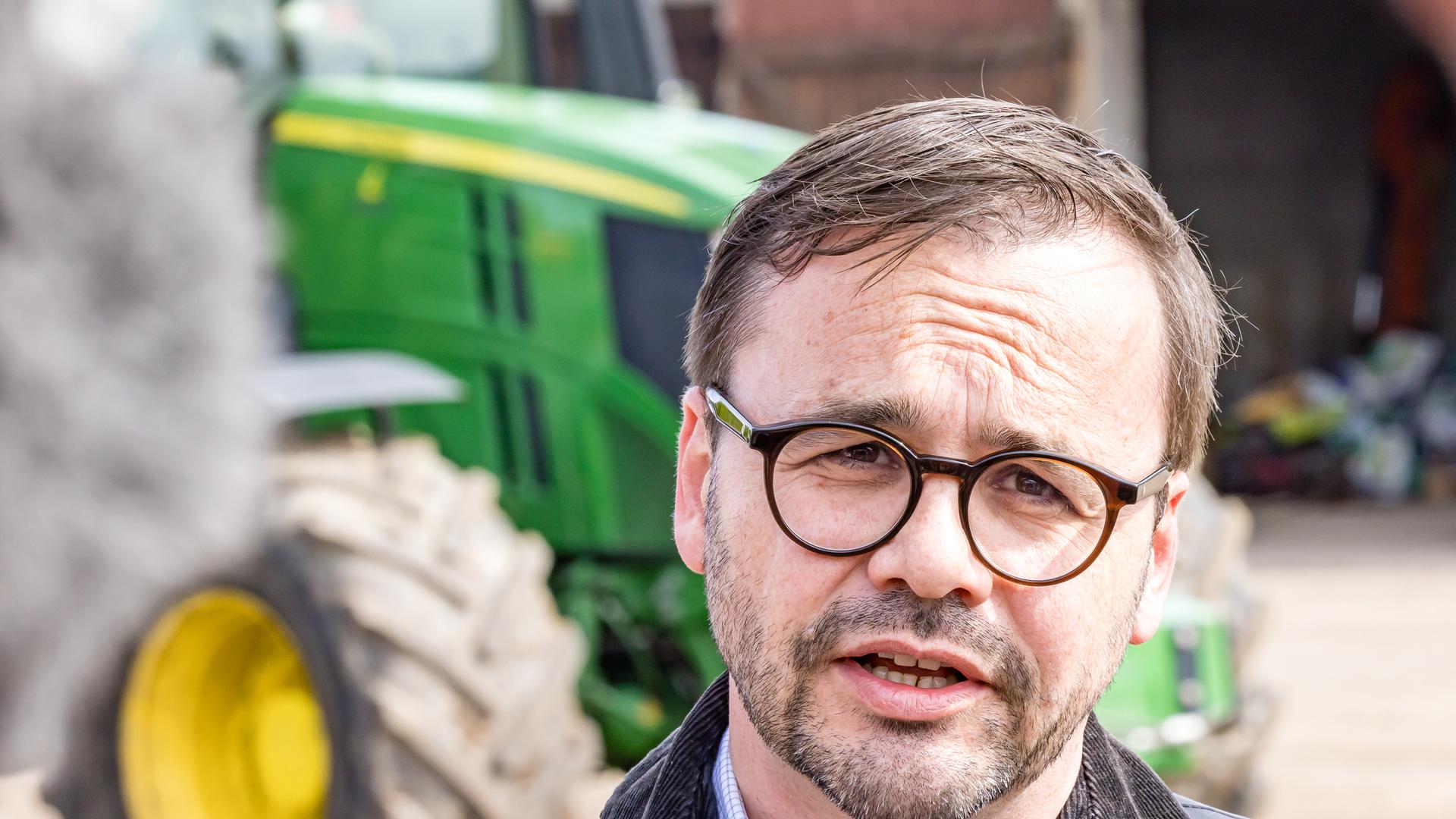 Brandenburgs Innenminister Jan Redmann (CDU) informiert sich auf einem vom Rinderdiebstahl betroffenen Hof in Herzberg. Hinter ihm steht ein grüner Traktor. 