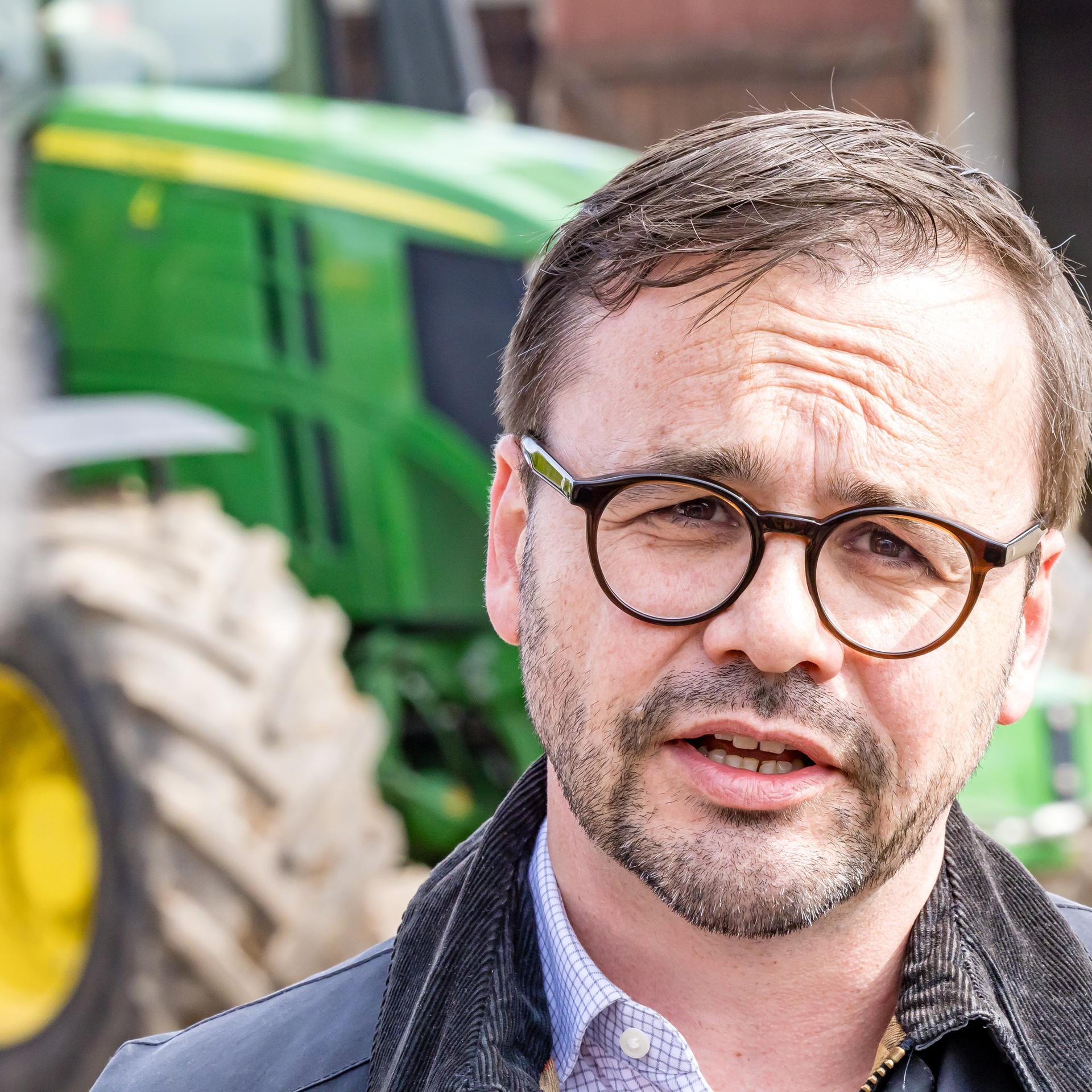 Brandenburgs Innenminister Jan Redmann (CDU) informiert sich auf einem vom Rinderdiebstahl betroffenen Hof in Herzberg. Hinter ihm steht ein grüner Traktor. 