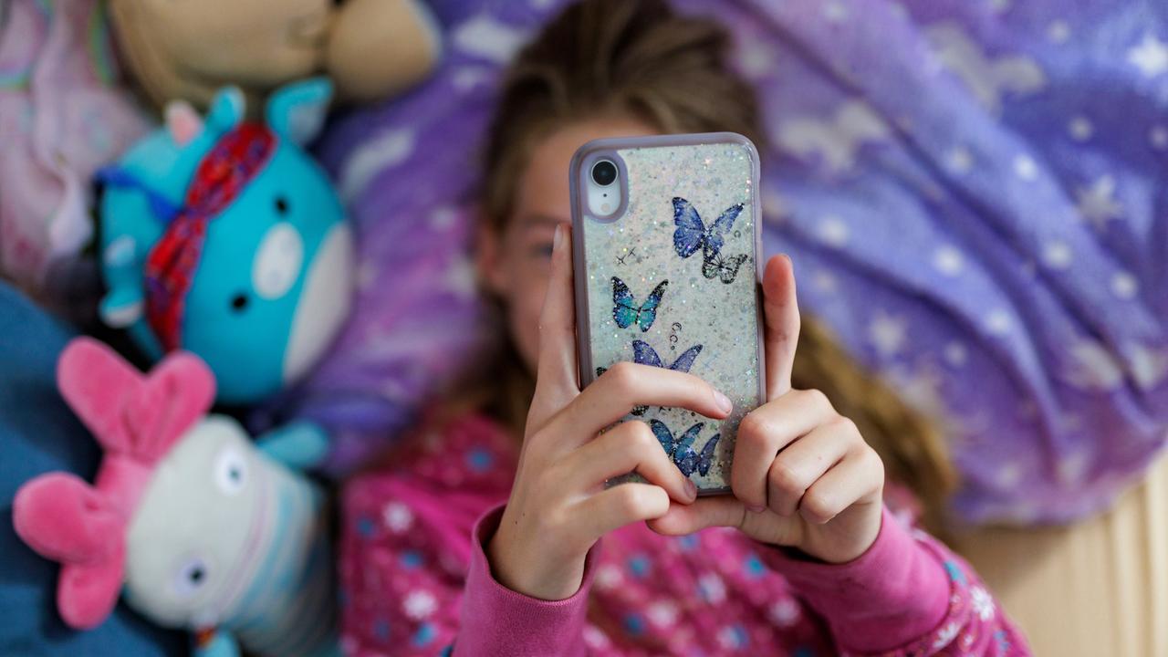 Ein Mädchen liegt in ihrem Bett und schaut auf ein Handy, das ihr Gesicht verdeckt.